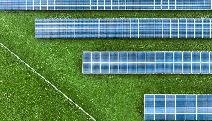 Aerial view of a field with several rows of solar panels arranged diagonally on a lush green grass background.