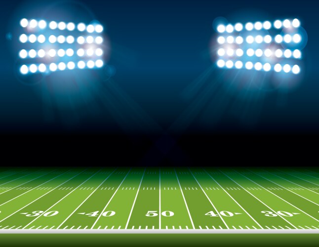 A brightly lit football field under stadium floodlights, with yard lines marked in white. The field is empty, and the night sky is dark above the illuminated scene.